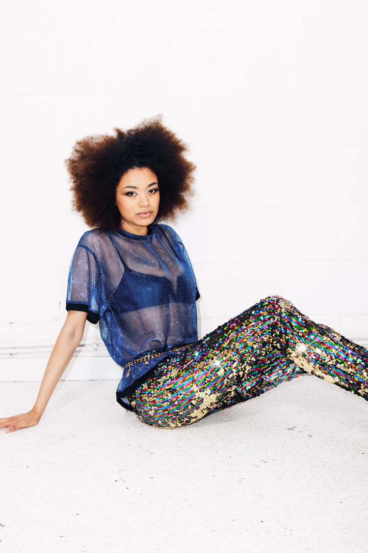 Woman wearing rainbow sequin pants and sheer blue top for festival outfit