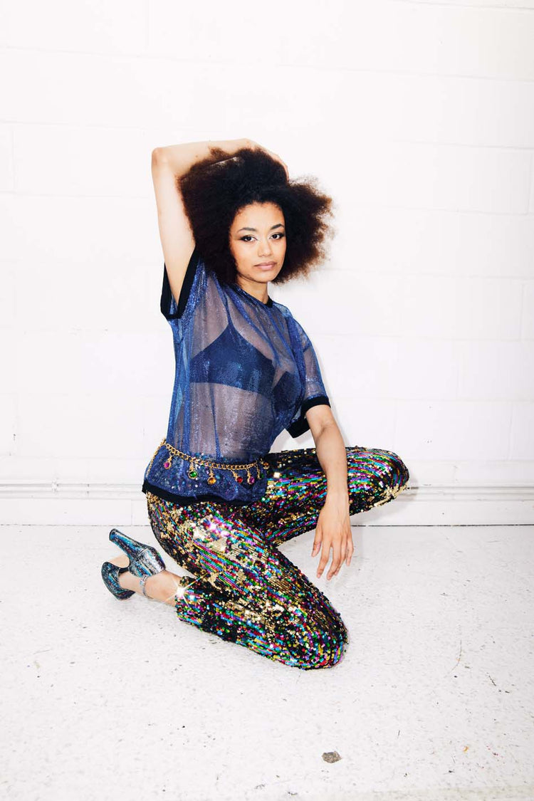 Woman wearing rainbow sequin pants and sheer blue t-shirt for party outfit