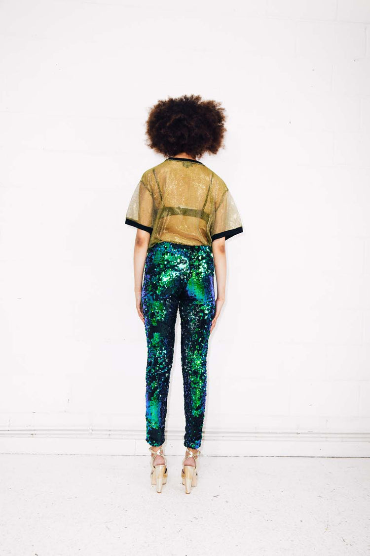 Woman wearing green sequin pants and gold sheer t-shirt at festival